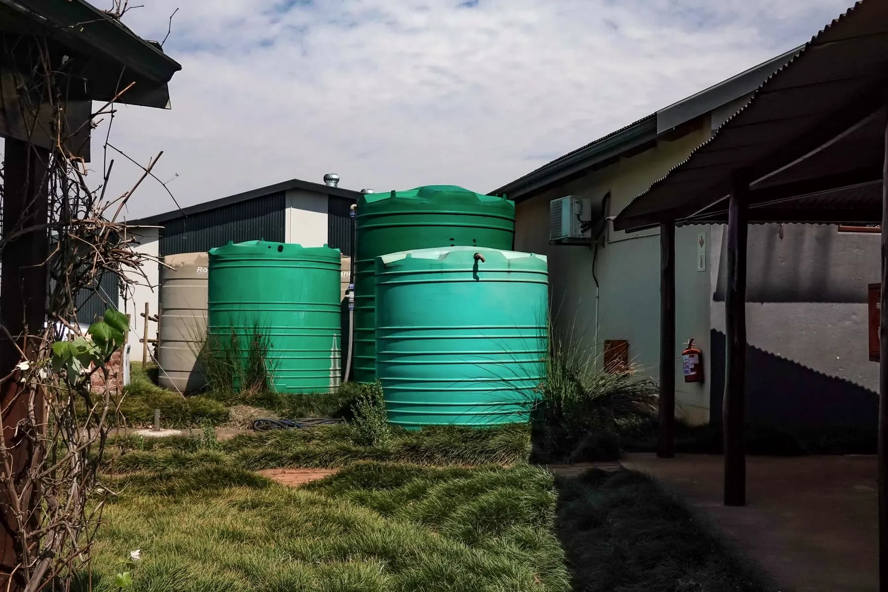Three green water storage tanks standing beside a farm building on a cloudy day
